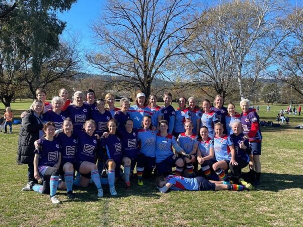 Group photo of two women's soccer teams, one in a purple jersey while the other in blue.