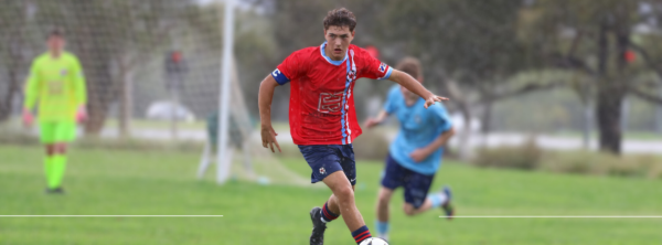 Boy running with a soccer ball with blue shirt opponent behind him.